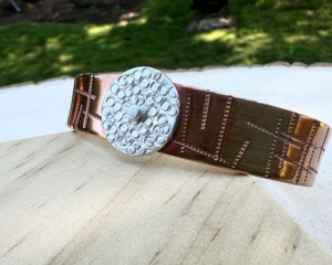 Copper cuff with a random stamped design with a sterling silver circle attached with a rivet