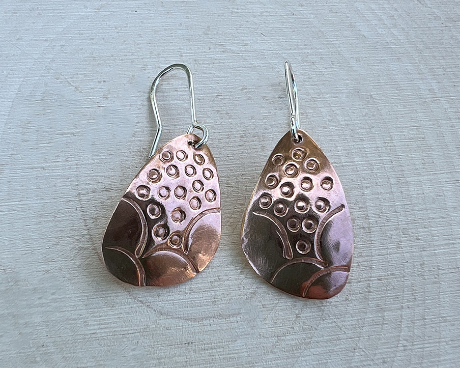 Teardrop shaped copper earrings with a hand stamped design, attached to sterling silver ear wires.