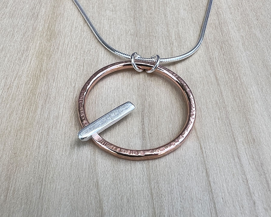 Copper wire shaped into a circle with a sterling silver bar attached. Sterling silver snake chain attached.